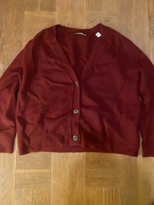 Vinröd kofta från Esprit - Säljer en vinröd kofta från Esprit med tre knappar framtill och ribbade muddar vid ärmslut och nederkant. Koftan är stickad och har en klassisk v-ringad design med lång ärm. Perfekt för lager-på-lager under höst och vinter. Den är i fint skick. En av lapparna är avdragen (se bild). Säljer för att den inte kommit till användning. Pris kan diskuteras.