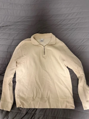 Beige half zip tröja från Zara - Säljer en stilren beige långärmad tröja från Zara med half zip framtill. Tröjan har en mjuk krage och är gjord i bomullsmaterial som känns skönt mot huden. Perfekt för dig som gillar enkel och clean stil.