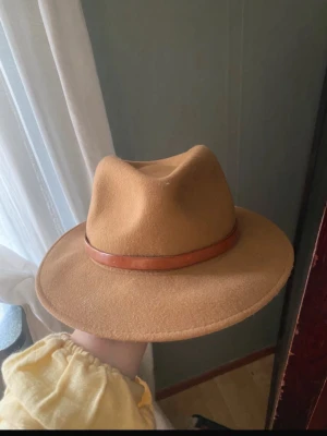 100 % bomull - Bilden visar en brun hatt med ett brunt band, ingen väst syns på bilden.