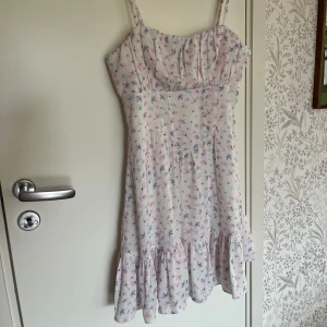 Blommig sommarklänning från NA-KD - Supersöt kort klänning med smala axelband från NA-KD. Vit med små blommor. Volang nertill och dragkedja i sidan. Nypris runt 300-400 kr men finns inte att köpa längre. Använd 2-3 gånger💓