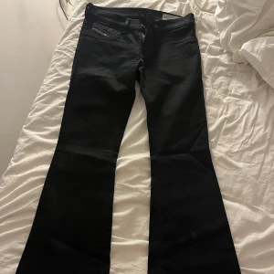 Svarta Diesel Livier-Flare jeans W28 L30 - Säljer ett par svarta Diesel Livier-Flare jeans med låg midja och super slim-flare passform. Jeansen har klassiska fem fickor, stretchigt material och snyggt utsvängda ben. Perfekta för dig som gillar en modern och cool siluett.