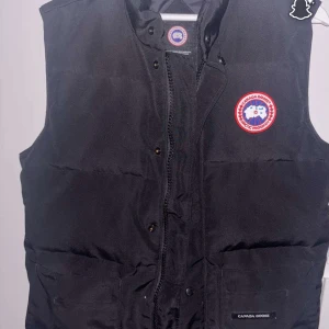 Svart dunväst från Canada Goose - Säljer en riktigt fet canada goose väst till ett bra pris, perfekt nu till kyligare dagar. Den kommer i bra skick utan några problem, vid frågor är det bara att skriva 