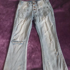 Ljusblå bootcut jeans med slitningar - Säljer ett par ljusblå jeans från Top Trend med bootcut-modell och snygga slitningar framtill och baktill. Jeansen har hög midja, tre knappar i gylfen och stora fickor fram. Perfekta för en avslappnad och trendig look. Kan diskutera pris