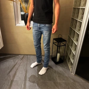 Replay Anbass - Säljer ett par Replay Anbass jeans i storlek 30/34 ljusblå tvätt med snygga slitningar och skinny passform. Klassisk femficksmodell med dragkedja och knapp, samt Replay-logga på bakfickan. Perfekta för dig som gillar smal siluett och mjukt stretchigt material.