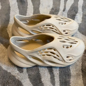 Beige adidas Yeezy Foam Runner(pris kan diskuteras) - Säljer ett par beige adidas Yeezy Foam Runner med futuristisk design och massor av hål för extra ventilation. Skorna är tillverkade i lätt syntetmaterial och har en chunky, rundad sula. Perfekta för dig som vill sticka ut med en unik och bekväm look.