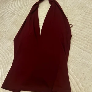 Vinröd halterneck topp med knyt - Säljer en vinröd halterneck topp med v-ringning och knyt i nacken. 