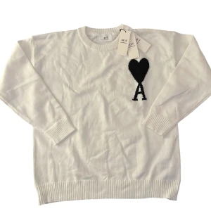 Vit stickad tröja från Ami Paris - Vit stickad tröja från Ami Paris med svart hjärta och bokstaven A broderat på bröstet. Klassisk rund halsringning, ribbade muddar och nederkant. Perfekt för dig som gillar stilrena och trendiga plagg med en twist. Har ej riktigt bestämt priset så kom med prisförslag!