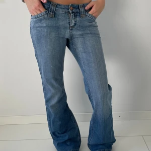 Blåa bootcut jeans  - Snygga blåa jeans bootcut passform och låg midja. Jeansen har klassisk femficksdesign, breda hällor och dekorativa sömmar på bakfickorna. Tillverkade i mjukt denim med lätt slitning för en cool vintagekänsla.