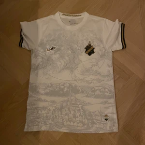AIK vit specialtröja Nike Modesto 32 - AIK fotbollströja från Nike i vitt med unikt grått stadsmotiv över hela framsidan. Klubbmärke och Nike-logga i guld, svarta detaljer på ärmarna och tryck med Modesto 32 på ryggen. Sparsamt använd och bra kvalitet! Tröjan är ej inköpt från AIK shop.