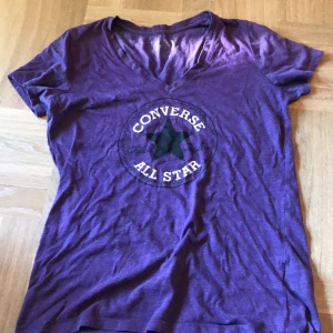 Lila Converse All Star t-shirt - Säljer en lila v-ringad converse tröja. Jag köpte den second hand men har själv inte använt den så jag vet inte hur använd den är, men är i ganska bra skick. Den är lite nopprig men det förstör inte intrycket av tröjan. Skriv innan du köper!!!!!