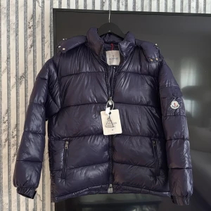 Moncler Maya mörkblå  - Hej säljer en helt ny moncler Maya vinter jacka i färgen mörkblå storlek M nya modellen helt oanvända klister märken på plastfickor på med nfc tag på sidan scan kod och artikelnummer jackan är helt ny och aldrig använd säljs så den va för stor för tjejen då jag beställde som present så fick köpa en ny . Både tjej o kille kan använda 