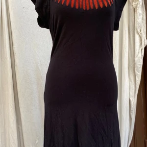 Vila Clothes svart klänning, storlek M - Svart klänning med dekorativa utskärningar fram och bak. Kortärmad och i en enkel modell. 92% viskos ﻿8 % elastan ﻿Längd: 98 cm ﻿Bystvidd: 43 cm. Katter finns inhemmet! 01