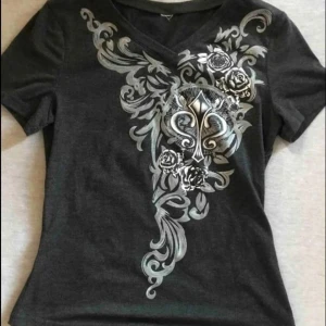 Svart topp - snygg svart t-shirt med v-ringning och silverfärgat tryck framsidan. tröjan sitter tajt och har korta ärmar. perfekt för dig som gillar edgy och detaljerade prints!! tröjan har använts några gånger bara 🩷