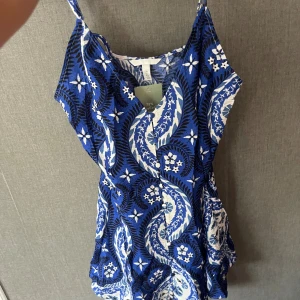 Blå och vit mönstrad klänning H&M S - Snygg kort klänning från H&M i storlek S med blått och vitt blommigt mönster. Klänningen har smala axelband och en lätt v-ringad hals. Materialet är mjukt och känns som bomull, perfekt för varma dagar. Den har en avslappnad passform och är superenkel att styla.