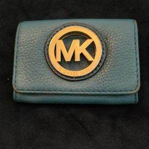 Plånbok från Michael Kors❣️ - Snygg blå plånbok från Michael Kors i skinn med stort guldfärgat MK-emblem på framsidan. Plånboken har tryckknappsstängning och flera fack för kort och sedlar. Perfekt storlek för att ha med sig överallt och ger en lyxig känsla med sin guldiga detalj. 7×11cm