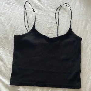 Svart ribbad linnetopp med tunna band - En svart ribbad linnetopp med dubbla tunna axelband och croppad passform. Köpt från lager 157 men lapparna tyvärr avklippta. Storlek: S men passar även M då materialet är väldigt stretchigt. 