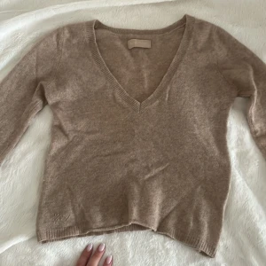 Beige v-ringad kashmirtröja från Zadig & Voltaire - Supermjuk beige kashmirtröja från Zadig & Voltaire med v-ringad hals och lång ärm. Tröjan har en klassisk, lite loose passform och ribbade muddar vid hals, ärmslut och nederkant. Perfekt för dig som gillar stilrena och lyxiga basics.