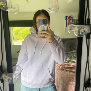 Ljuslila hoodie med blå fjäril - Säljer en ljuslila hoodie med stor blå fjäril och vit text på ryggen. Hoodien har huva med snörning och en klassisk känguruficka framtill. Perfekt för dig som gillar unika tryck och sköna, avslappnade plagg.