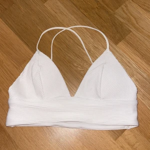 Vit ribbad bikiniöverdel - Supersnygg vit bikiniöverdel med ribbad struktur och smala axelband som korsas i ryggen. Triangelformade kupor och bredare band under bysten. Banden är justerbara och kuporna är uttagbara. Säljer då den tyvärr är för liten för mig 💗