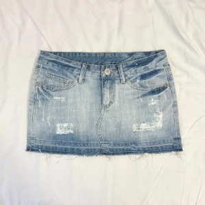 Lågmidjad jeanskjol med revor  - 2000s low waist ljusblå jeanskjol med snygga slitningar i jättebra skick, mått på sista bilderna 