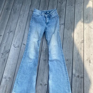 Bootcut jeans från Divided H&M, ljusblå - Ljusblå bootcut jeans från Divided H&M med slitningar på låret och klassiska femficksdetaljer. Jeansen har hög midja och är tillverkade i bomull. Perfekta för dig som gillar en retro vibe och vill ha ett par jeans med lite extra attityd.