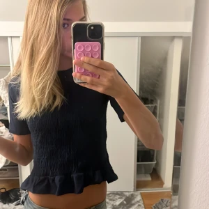 Mörkblå topp med volangkant - Supersöt mörkblå topp med smockad framsida och volang längst ner. Kortärmad och croppad modell som ger en trendig vibe. Perfekt att styla med jeans eller kjol för en chill look. Kontakta mig vid köp❣️