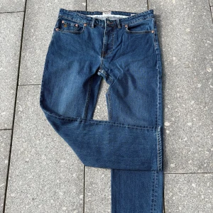 Blå jeans från Morris Stockholm - Snygga blå jeans från Morris Stockholm med klassisk femficksdesign och bruna kontrastsömmar. Jeansen har en rak passform och är tillverkade i slitstarkt bomullsjeans. Liten guldfärgad detalj på myntfickan och läderpatch bak i midjan.
