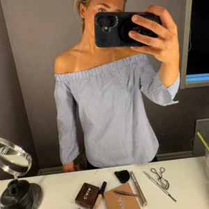 Randig offshoulder skjorta från Zara - Säljer en blåvit randig offshoulder skjorta från Zara Woman. Skjortan har trekvartsärmar och elastisk kant upptill för en snygg passform. Perfekt för dig som gillar en trendig och avslappnad stil.