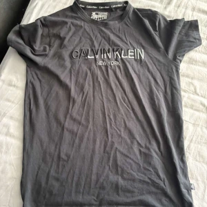 Svart Calvin Klein t-shirt i bomull - Svart t-shirt från Calvin Klein med broderad logga och texten 'New York' på bröstet. Klassisk rund halsringning och korta ärmar. Tillverkad i mjuk bomull för en skön känsla. Perfekt för en clean och stilren look.