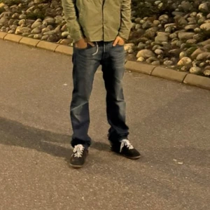 Levi's 501 blå jeans straight fit - Klassiska Levi's 501 jeans i blå denim med raka ben och normal passform. Jeansen har fem fickor, knappgylf och snygga slitningar för en avslappnad look. Perfekta för dig som gillar tidlös stil och vill ha ett par jeans som funkar till allt.