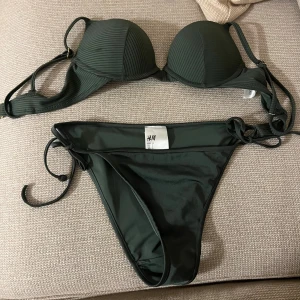 Mörkgrön bikini från H&M med snörning - Snygg mörkgrön bikini från H&M med ribbad push-up överdel och klassiska bikinitrosor med knyt i sidorna. Perfekt för strandhäng och poolparty. Materialet är mjukt och följsamt syntet som torkar snabbt. Stilren och enkel design som passar dig som gillar att sticka ut med färg. (Överdelen på bikinin är storlek 70B)