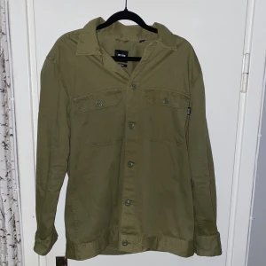 Olivgrön overshirt från Only & Sons - Snygg olivgrön overshirt från Only & Sons med klassisk krage och två bröstfickor med knappar. Perfekt att bära öppen eller stängd för en avslappnad look.