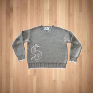 Grå stickad tröja med dollartryck - Grå stickad tröja från Sthlm Misc med stort dollar-tecken framtill och texten 'buy happiness' på ryggen. Tröjan har rund hals, ribbade muddar och vita detaljer vid ärmslut och nederkant. Perfekt för dig som gillar streetstyle och statement-plagg. S-xl finns inne