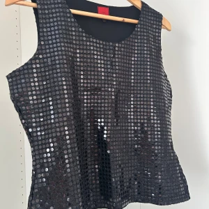 Svart paljettopp från JDY - Snygg svart ärmlös topp från JDY, täckt med glittrande paljetter som ger en riktigt festlig look. Toppen har rund halsringning och är figursydd för en smickrande passform. Perfekt för dig som vill sticka ut med lite extra bling. Har 2st en i svart och guld🤩🤩🤩