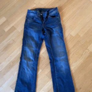 G-Star RAW Midge Bootcut Jeans blå - Snygga blå bootcut jeans från G-Star RAW, modell Midge. Klassisk femficksdesign med coola slitningar och kontrastsömmar. Jeansen har normal passform och är tillverkade i slitstark denim. Perfekta för dig som gillar en tidlös och avslappnad look.