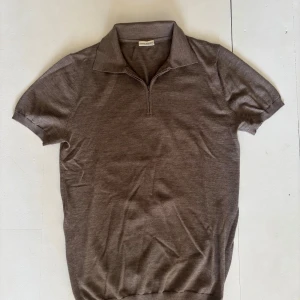 Brun pikétröja från John Henric - Säljer en brun pikétröja från John Henric med kort ärm och klassisk krage. Tröjan har en half zip-dragkedja framtill och är tillverkad i mjukt stickat material. Perfekt för en stilren och avslappnad look.