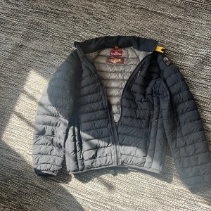 Svart lättviktsdunjacka Parajumpers - Snygg svart lättviktsdunjacka från Parajumpers med quiltad design och dragkedja framtill. Jackan har klassisk passform, lång ärm och ikonisk logga på axeln. Perfekt för dig som vill ha en stilren och funktionell jacka med sportig känsla. storlek y-l men skulle säga att den är som en M. Passar dig som är upp till 185cm. 