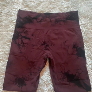 Mörkröda träningstights - Snygga mörkröda träningstights shorts med svart marmorliknande mönster. Högmidjade och tillverkade i stretchigt material med 95% polyamid och 5% elastan.