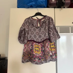 Mönstrad blus från Odd Molly - Supersöt blus från Odd Molly med unikt mönster i lila, grått och inslag av gult och rosa. Blusen har vida trekvartsärmar, knytning i nacken och en lös passform. Materialet känns lätt och flowy, perfekt för dig som gillar boho-vibes och färg. Storlek 1 som enligt deras storleksguide motsvarar en storlek S. Fint skick, men den är något mer använd. 100% silke, tyget är fortfarande fin men kanske kan kännas något konstigt. 