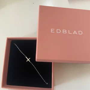 Silverarmband med kors från Edblad - Stilrent armband i silver från Edblad med en tunn kedja och ett minimalistiskt kors som detalj. Perfekt för dig som gillar enkel och modern design. Levereras i original ask.