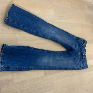 Blå bootcut jeans med broderade fickor - Säljer ett par blå bootcut jeans med snygga broderade detaljer på bakfickorna och klassisk femficksdesign. Jeansen har hög midja och är tillverkade i jeansmaterial med en lätt tvättad look. Perfekta för dig som gillar en retro vibe och vill sticka ut lite extra.