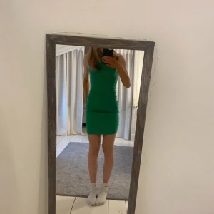 Grön ärmlös kortklänning - Snygg grön ärmlös klänning med tight passform och rund hals. Klänningen är kort och har en enkel, stilren design som framhäver figuren. Perfekt för dig som gillar minimalistisk stil och vill sticka ut med en stark färg.