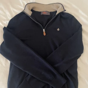 Marinblå merinoulltröja från Morris - Säljer en stilren marinblå tröja från Morris i 100% merinoull. Tröjan har half zip med snygg dragkedja och kontrastfärgad insida på kragen. Broderad logga på bröstet och långa ärmar. Perfekt för dig som gillar klassisk och clean stil.