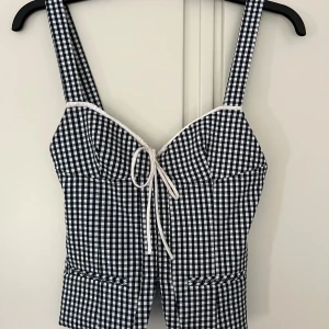 Rutig korsettopp från Zara XS - Supersöt svartvit rutig korsettopp från Zara med breda axelband och vit snörning framtill.  Använd max 3 gånger. Säljer pga den är för liten för mig. Hör av er om ni vill ha fler bilder.