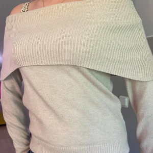Beige offshoulder stickad tröja Lindex - Superfin beige stickad tröja från Lindex med offshoulder-design och bred ribbad kant upptill. Långärmad och mjuk, perfekt för dig som gillar en stilren och trendig look. Snygg att matcha med jeans eller kjol!