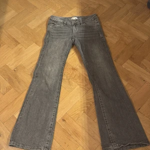 Grå bootcut jeans med broderade fickor - Snygga grå jeans med bootcut passform och coola broderade detaljer på bakfickorna. Jeansen har klassisk femficksdesign, knappstängning och är tillverkade i ett mjukt denimtyg. Perfekta för dig som gillar en avslappnad men ändå unik stil.