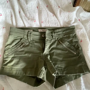 Olivgröna shorts från 365 med dragkedjor - Snygga olivgröna shorts från 365 med två dragkedjefickor framtill och klassiska bakfickor. Modellen har bälteshällor och knappstängning. Perfekta för varma dagar och enkel att matcha med det mesta. Materialet känns mjukt och bekvämt.