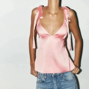 Rosa satin linnetopp med knytband - Supersöt rosa linnetopp i satin med smickrande v-ringning och knytband på axlarna. Toppen är ärmlös och har en lätt glansig finish som ger en lyxig känsla. Perfekt att styla med jeans eller kjol för en trendig look. Använd 1 gång endast!!!