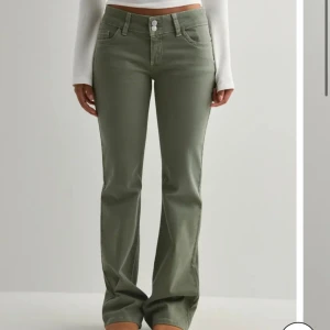 Olivgröna bootcut jeans med detaljer - Snygga olivgröna jeans med bootcut-snitt och coola sömdetaljer på bakfickorna. Byxorna har normal midja, klassisk femficksdesign och stängs med två knappar framtill. Perfekta för dig som vill ha en avslappnad men trendig look. Säljer då dem är förstora för mig. Prislapp kvar.