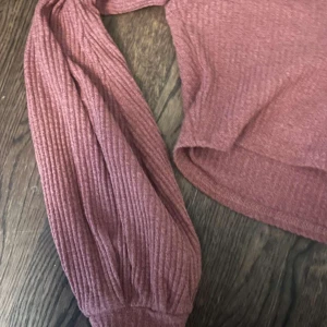 Rosa ribbad croppad topp med knappar - Superfin croppad topp i en dämpad rosa färg med ribbad struktur. Toppen har långa ärmar, v-ringning och knappar framtill. Perfekt för dig som gillar en chill men ändå snygg stil.